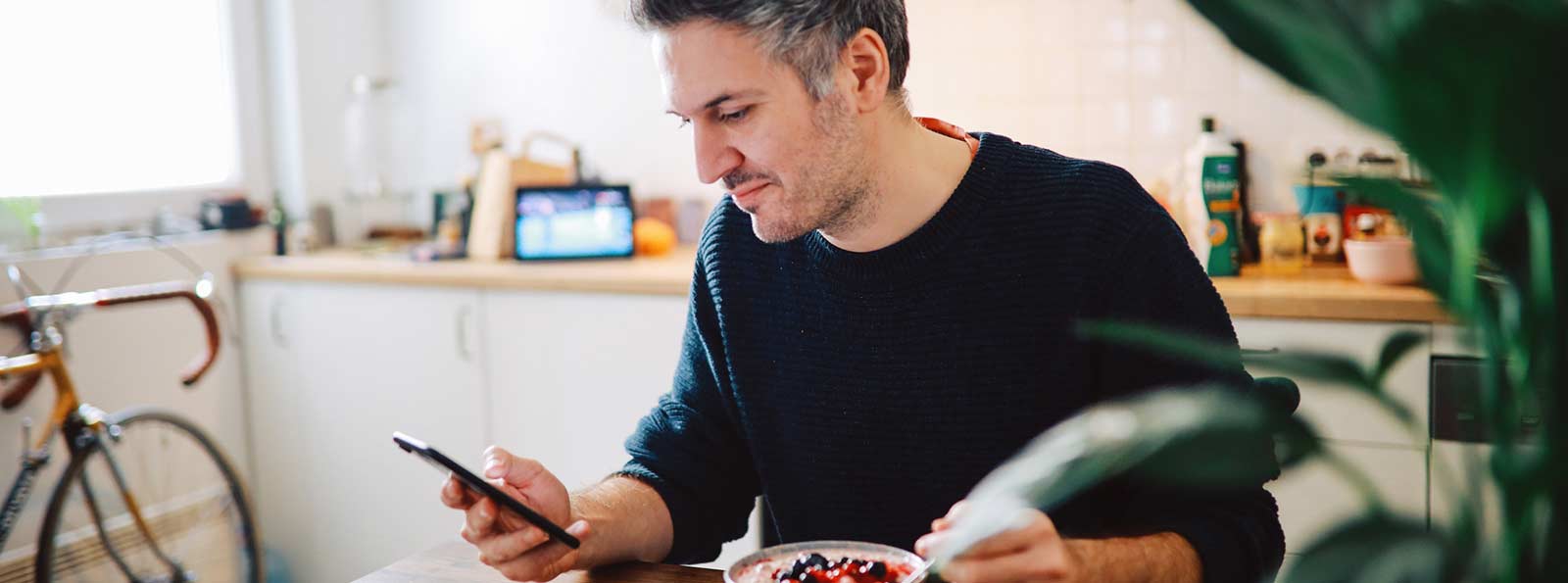 Man looking at phone while eating breakfast at home.