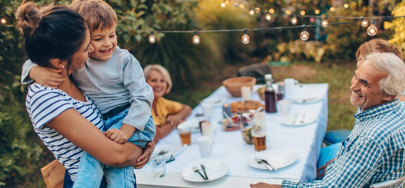 Mom holding son with parents at backyard dining table.