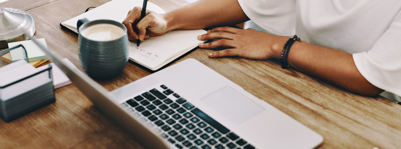 Woman writing at desk near laptop.