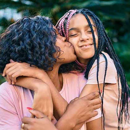 Mom kissing daughter outdoors.